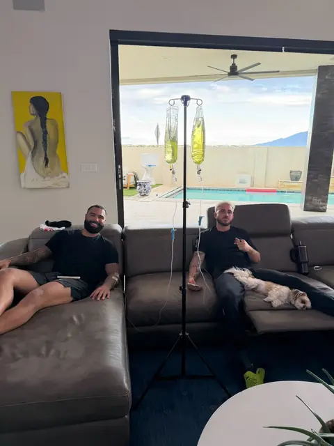 Two clients relaxing on a sectional sofa during IV hydration, with a pool visible through the patio doors