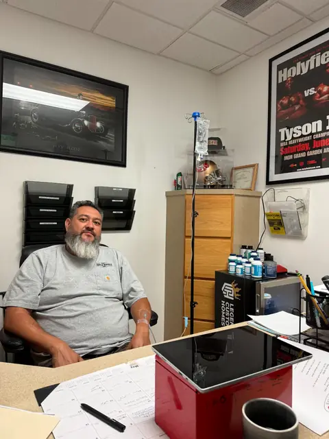 A man receiving an IV drip at his office desk while he works